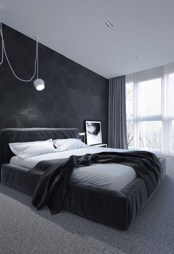 a stylish minimalist bedroom with a geometric accent wall, an upholstered black bed and a white pendant lamp