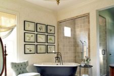 a stylish vintage bathroom with a gallery wall, a black clawfoot tub, a unique pendant lamp and some elegant furniture