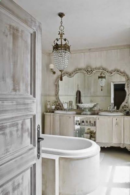 a super elegant neutral bathroom with a gorgeous crystal chandelier, a clad tub and an ornate mirror over the vanity