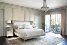 a very elegant Parisian bedroom with a printed rug, a chic upholstered bed, a crystal chandelier and mirror nightstands