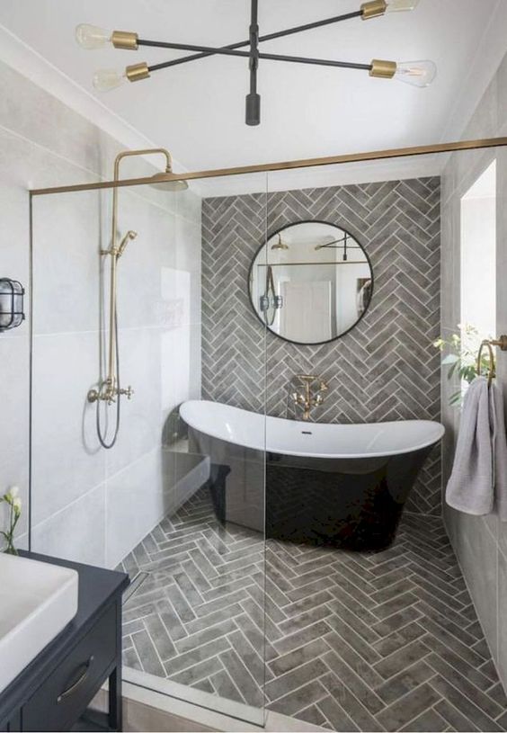 an elegant bathroom with grey tiles, a black tub, gilded touches, a black vanity and a round mirror looks super chic