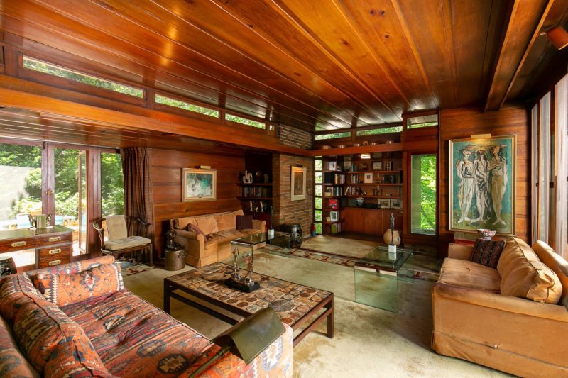 The living room is decorated with chic vintage and modern furniture, there's much warm colored wood and lots of windows