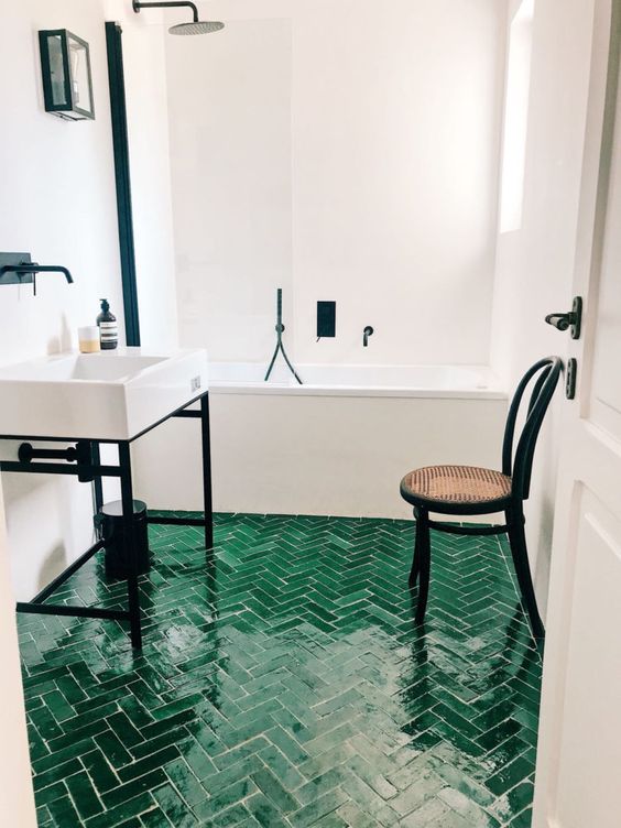 a neutral bathroo spruced up with dramatic black touches and an emerald tile floor with a herringbone pattern