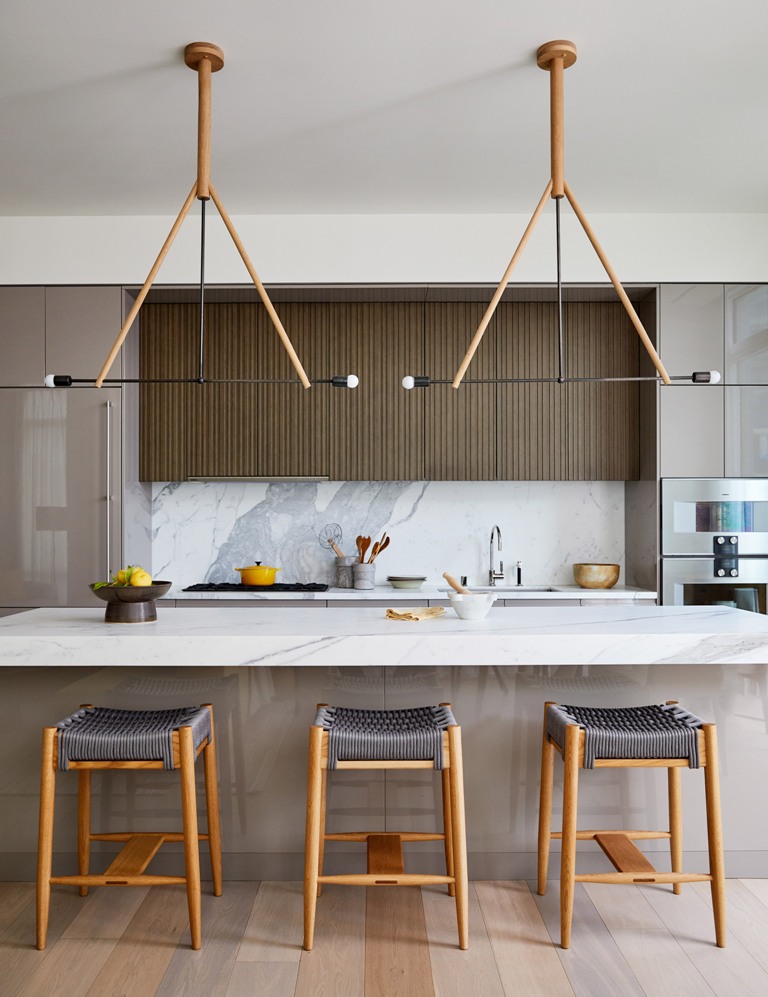 The kitchen is done with sleek cabinets, a marble backsplash and kitchen island and woven chairs