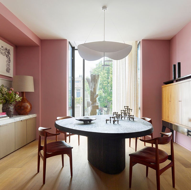 A dining room with a statement wooden dining table and a gorgeous chandelier features also pink walls