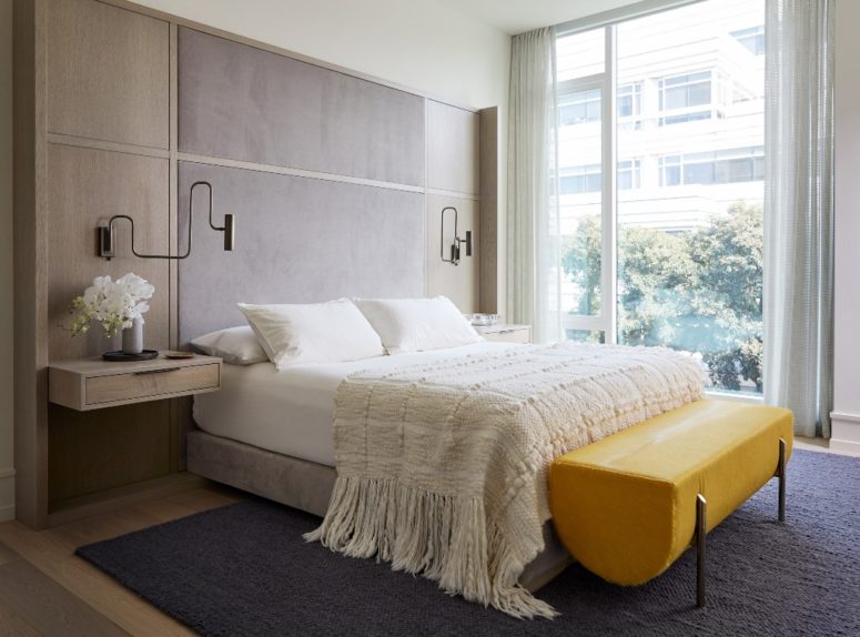 The bedroom is done with a floating bed, floating nightstands and a statement yellow bench of leather