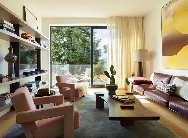 The living room is bright and bold, with pink chairs and a leather sofa plus an entrance to the terrace