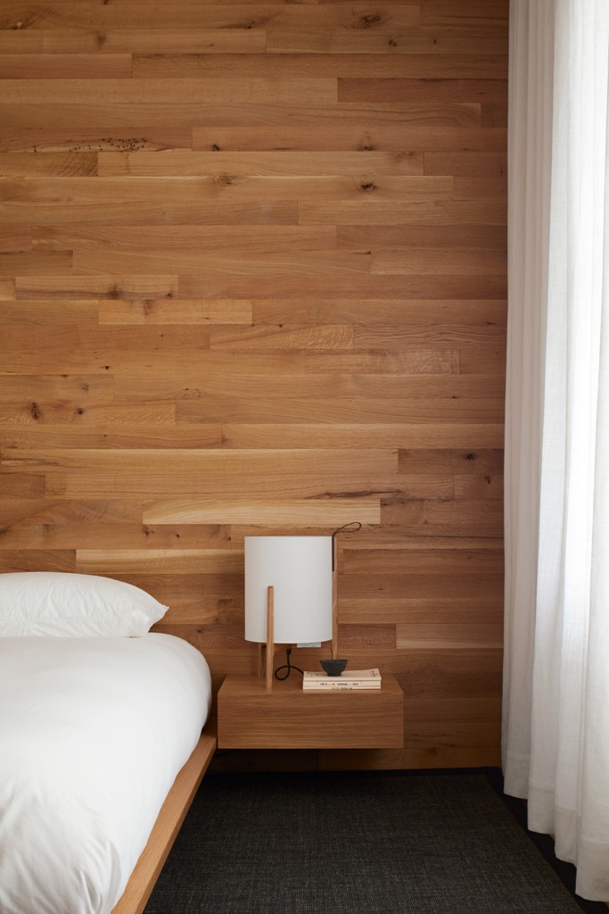 The master bedroom is done with a statement wall of wood and floating nightstands plus a floating bed, it's all neutral