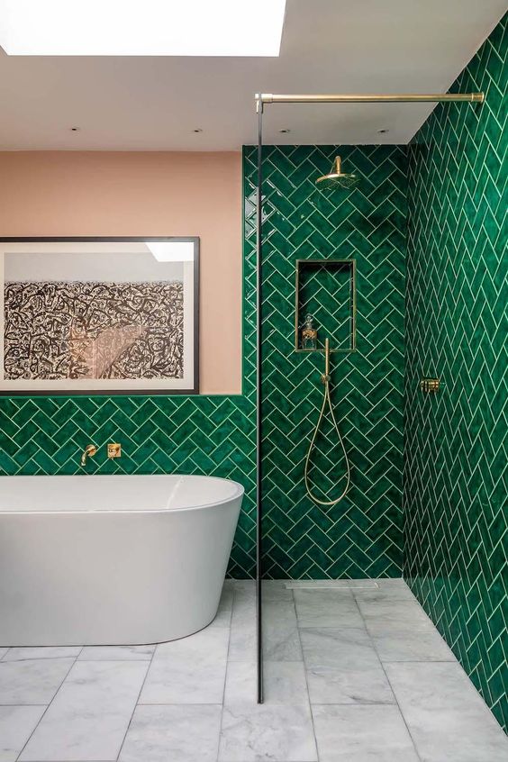 a bold bathroom with emerald tiles clad in a herringbone pattern and blush touches