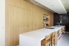 08 The kitchen is done with light-colored wooden cabinets, a large and long white kitchen island with an eating space