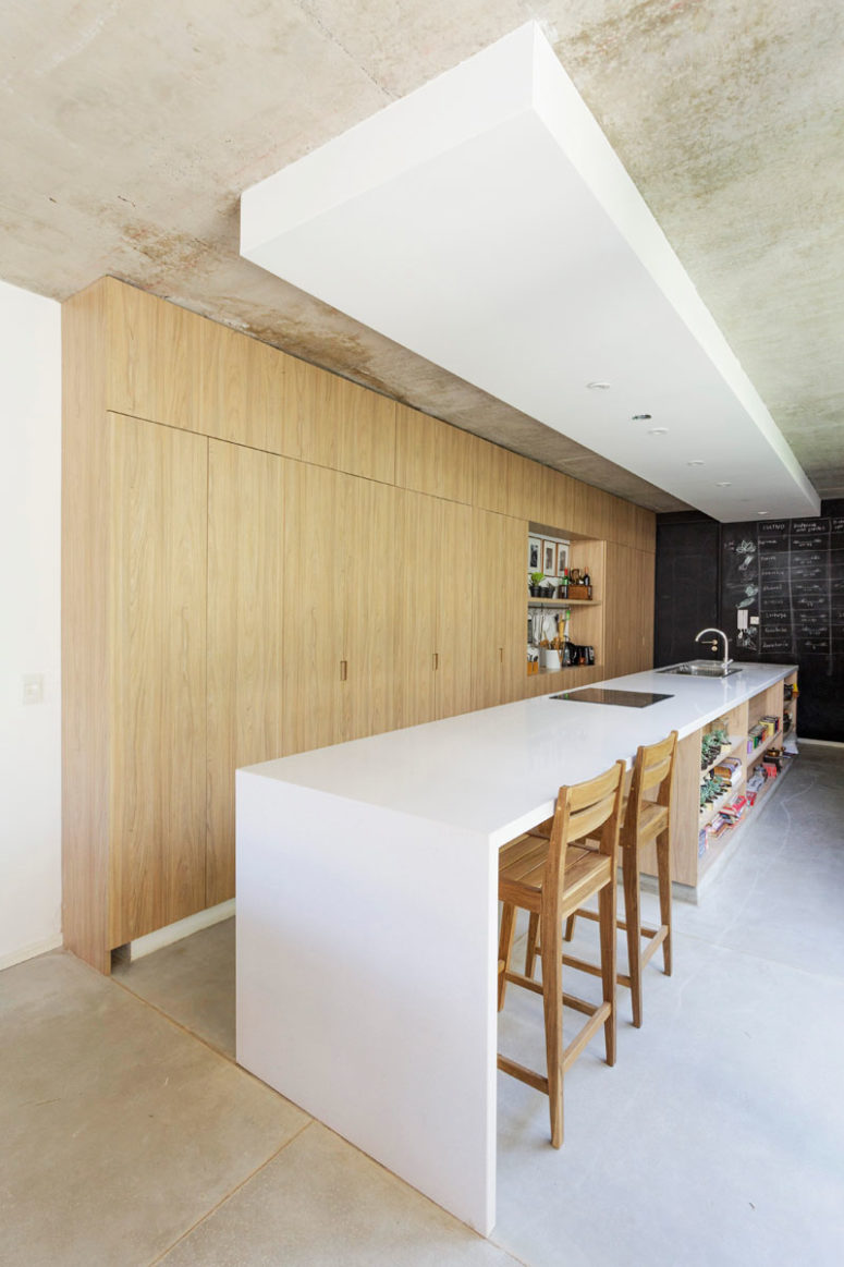 The kitchen is done with light-colored wooden cabinets, a large and long white kitchen island with an eating space