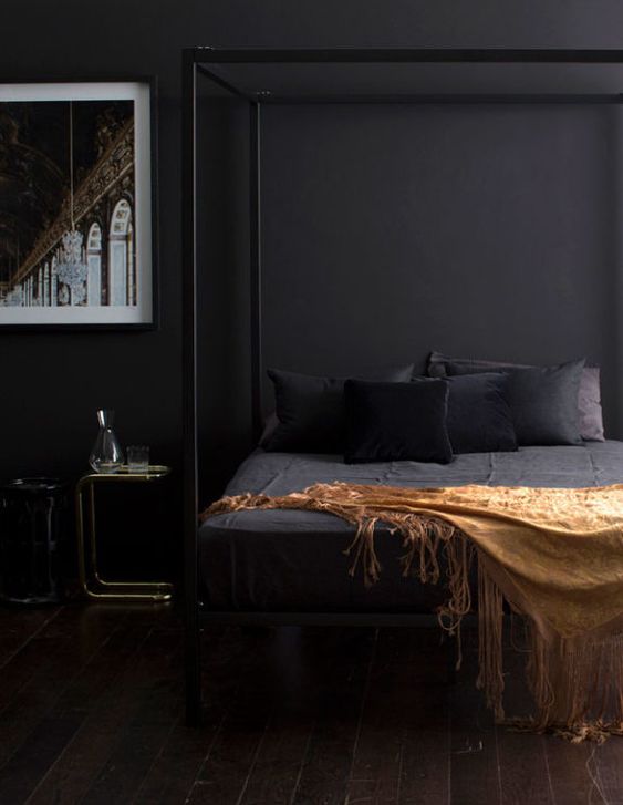 an elegant and moody bedroom with black walls, a framed bed and a statement artwork looks very relaxing