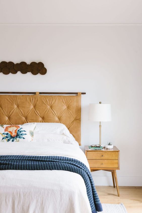 a hanging amber tufted leather headboard achoes with the nightstand and adds a warming up feel to the space