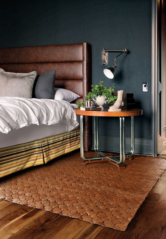a brown leather padded wingback headboard, a matching rug and a wooden top nightstand warm up the moody bedroom