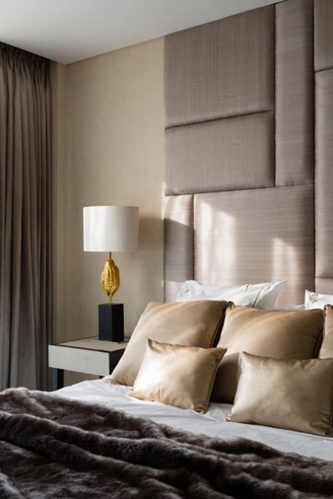 a beige padded upholstered headboard with a geometric pattern comes up to the ceiling and makes an elegant statement