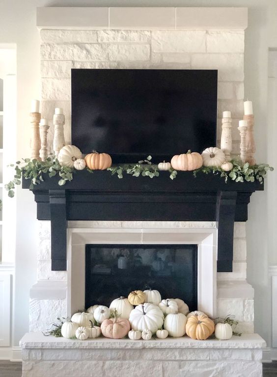a fireplace decorated with muted and neutral pumpkins, foliage and candles in elegant wooden candleholders