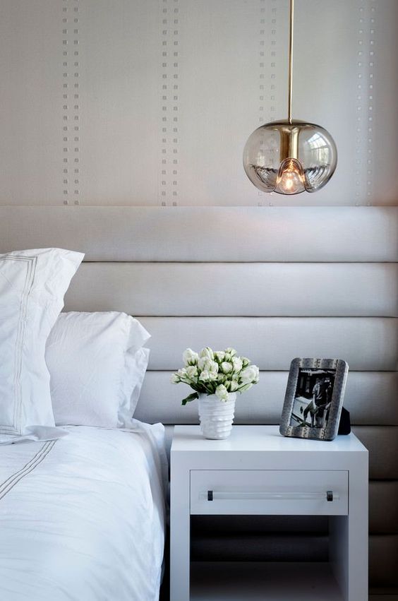 A glass pendant lamp with an eye catchy shape and gold touches spruces up a neutral bedroom