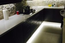 22 a dark kitchen featuring under the cabinet lights and over the countertop lights as ambient lighting