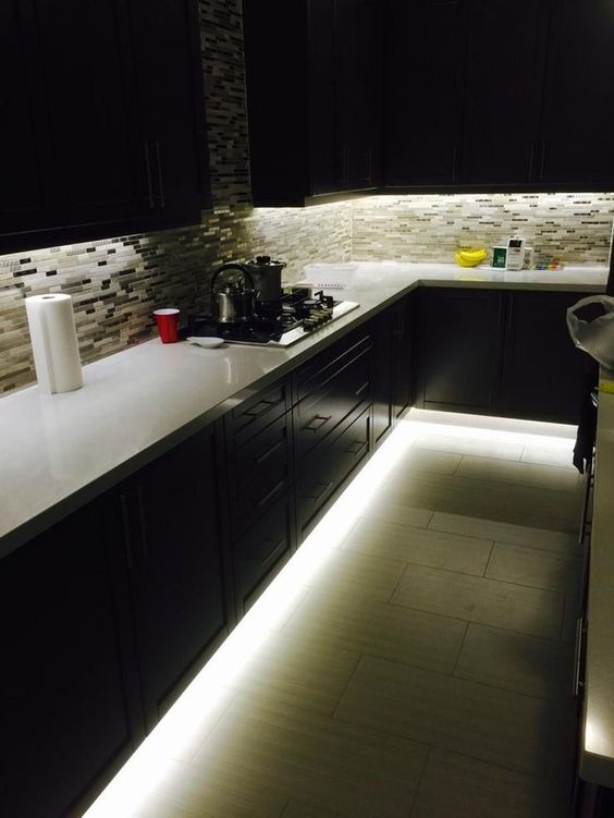 a dark kitchen featuring under the cabinet lights and over the countertop lights as ambient lighting