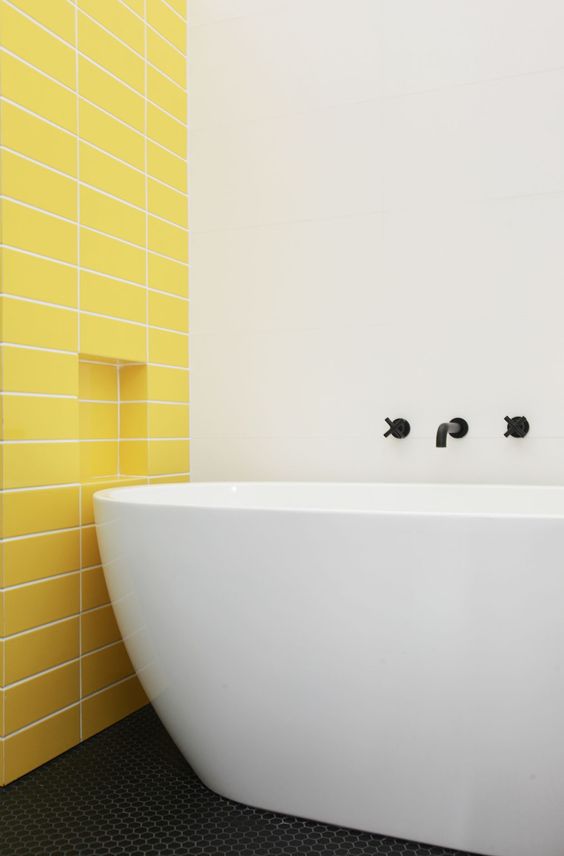 a minimalist bathroom with a statement yellow tile wall and a neutral and sleek bathtub