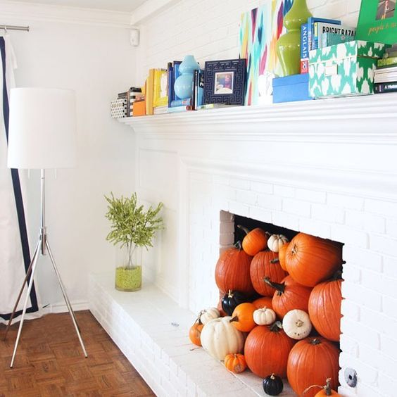 a non-working fireplace filled with various pumpkins for the fall and coming Halloween