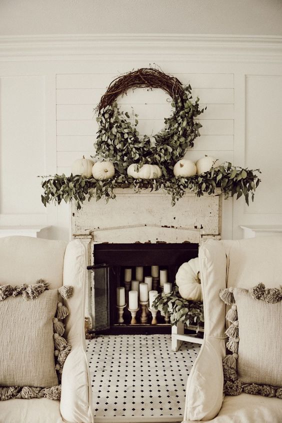 a mantel styled with greenery, white pumpkins and a large wreath of wine and greenery