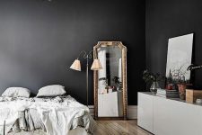 a Parisian bedroom with black walls, a bed with neutral bedding, a credenza, a mirror with an oranted frame and decor