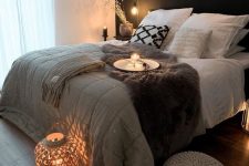 a Scandinavian bedroom with a black accent wall, a bed with neutral bedding, nightstands, lamps, lights and lanterns