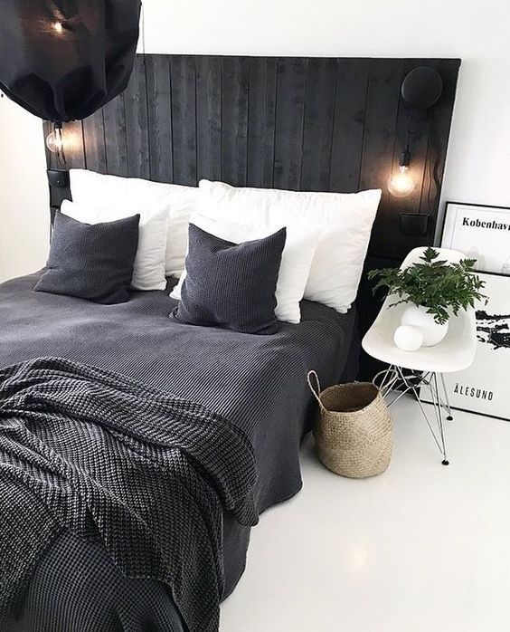 a Scandinavian bedroom with a black bed with an extended headboard, black and white bedding, a chair and a basket