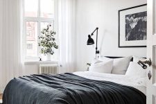 a Scandinavian bedroom with molding, a black bed with monochromatic bedding, a black lamp and some greenery