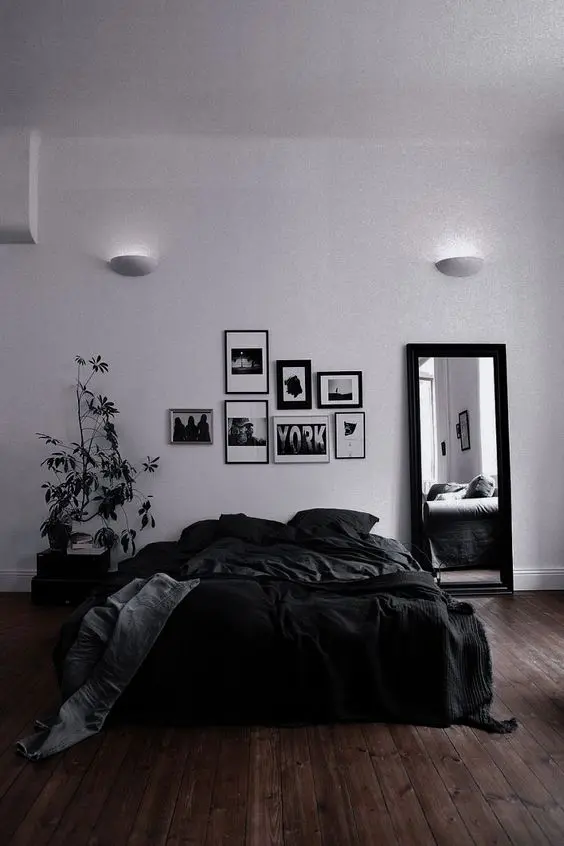 a black and white bedroom with a black bed and bedding, a black and white gallery wall and some plants