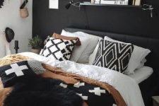 a boho bedroom with a black accent wall, a black bed and monochromatic bedding, a ledge with art and some wall decor