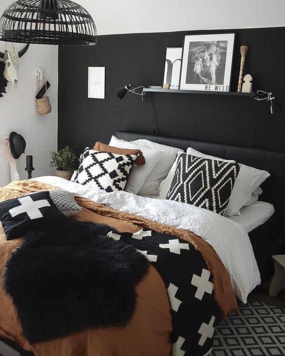 a boho bedroom with a black accent wall, a black bed and monochromatic bedding, a ledge with art and some wall decor