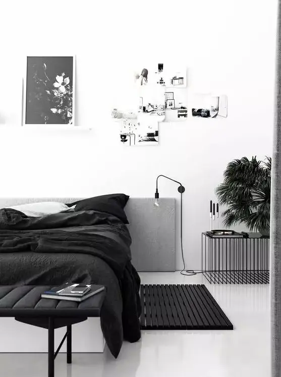 a catchy monochromatic bedroom with a white bed and black bedding, a black upholstered bench and a black table