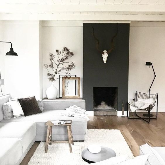 a chic Scandinavian living room with a blakc fireplac,e neutral furniture, wooden touches and greenery here and there