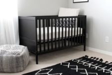 a chic nursery with a black crib, a printed rug, wooden shelves and a pretty artwork for a simple andd cozy space