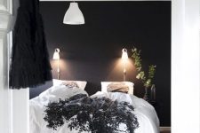 a classy Scandinavian bedroom with a black accent wall, a black bed with contrasting bedding, lamps and lights