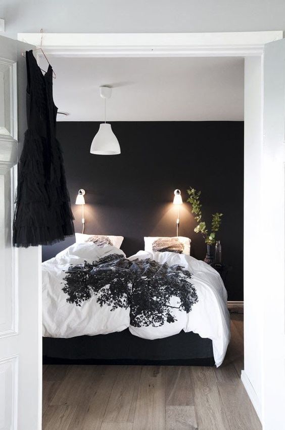 a classy Scandinavian bedroom with a black accent wall, a black bed with contrasting bedding, lamps and lights