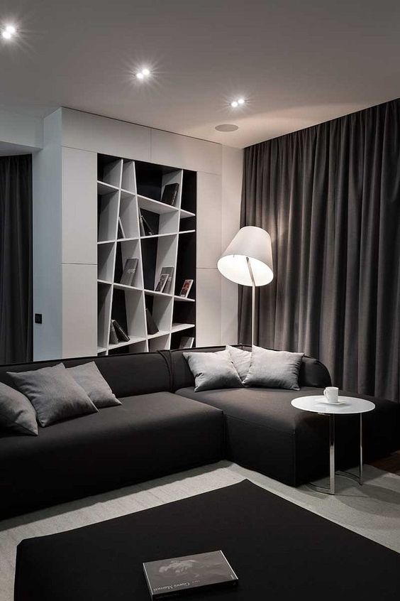 A contemporary black and white living room with a built in geometric shelf, a sectional sofa and a black ottoman