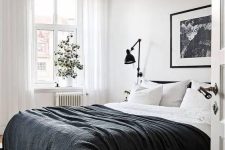 a contrasting Scandinavian bedroom with a black bed and black and white bedding, an artwork, black sconces and potted greenery