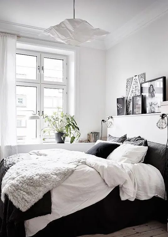 a contrasting bedroom with a black bed with black and white bedding, a ledge gallery wall and a pendant lamp