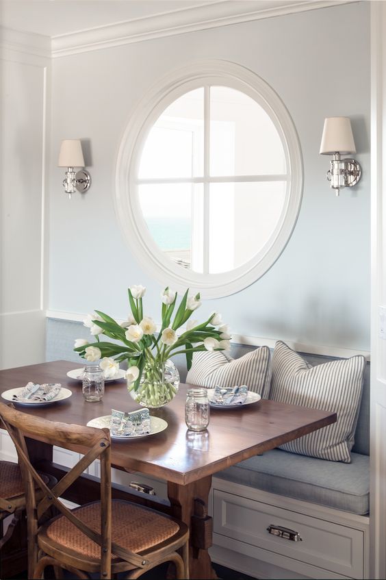 a cozy dining nook with a porthole window and wall lamps looks very refined and very chic