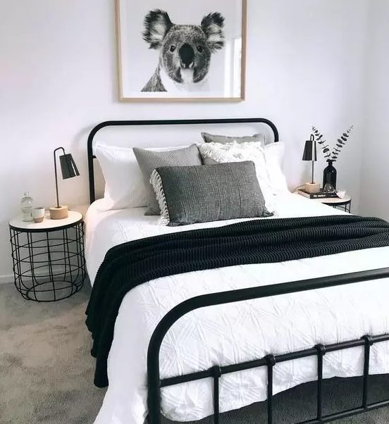 a cozy small bedroom in black and white, with a black metal bed, monochromatic bedding and a stylish industrial nightstand