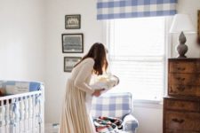a cute famrhouse nursery with lot sof blue plaid, a stained dresser, a neutral rug and a white vintage crib