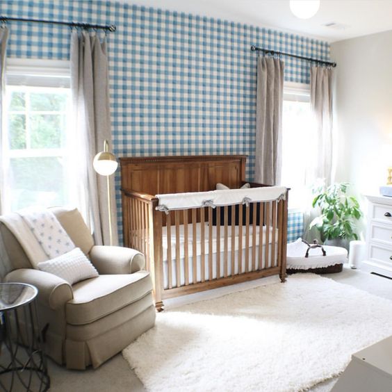a cute farmhouse nursery with a blue plaid wall, a stained crib, vintage furniture, grey curtains and a creamy rug