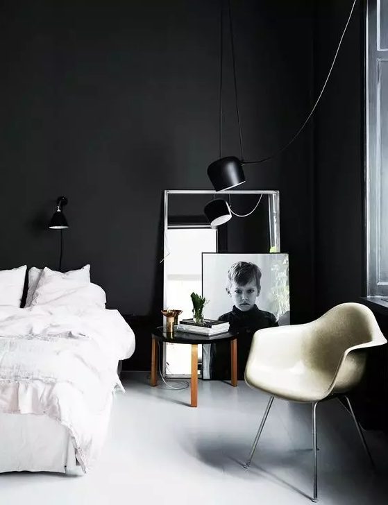 a laconic black and white bedroom with black walls, a bed with white bedding, a white leather chair and a mirror