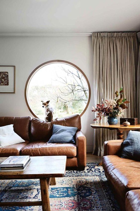 a large round window with wooden framing perfectly matches the chic living room and its color scheme