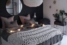 a lovely bedroom with a black accent wall, a bed with neutral bedding, a pendant lamp and lights and a jute rug
