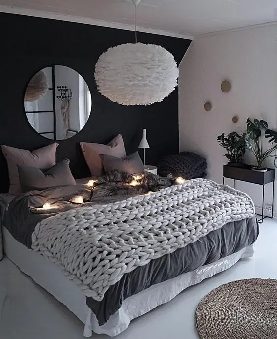 a lovely bedroom with a black accent wall, a bed with neutral bedding, a pendant lamp and lights and a jute rug
