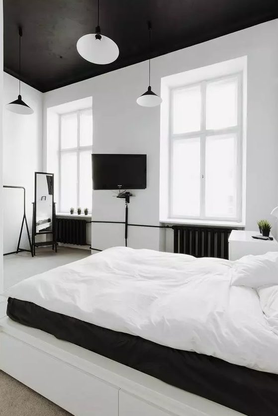 a minimalist bedroom done in black adn white, with a black ceiling, piping and pendant lamps plus white bedding
